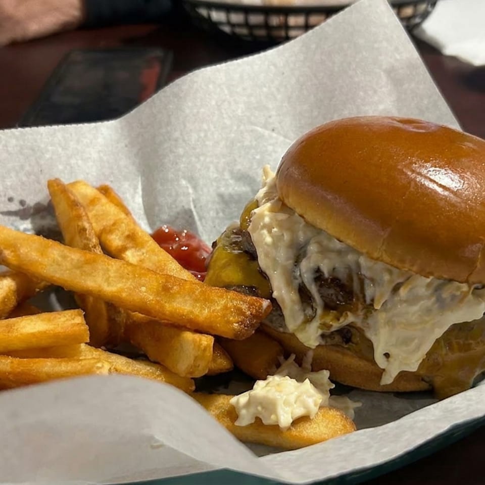 Cheeseburger with melted cheese and golden fries served in a paper-lined basket at a restaurant table.