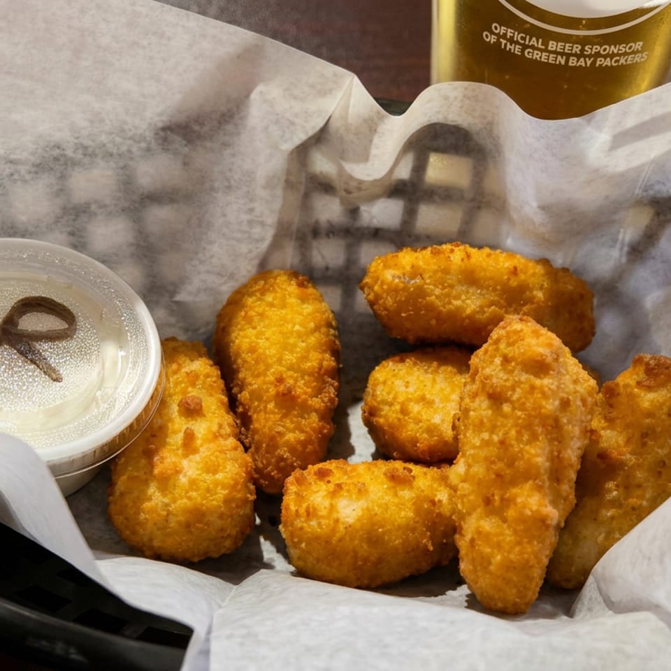 Basket of golden fried cheese curds with dipping sauce beside a beer on a restaurant table.